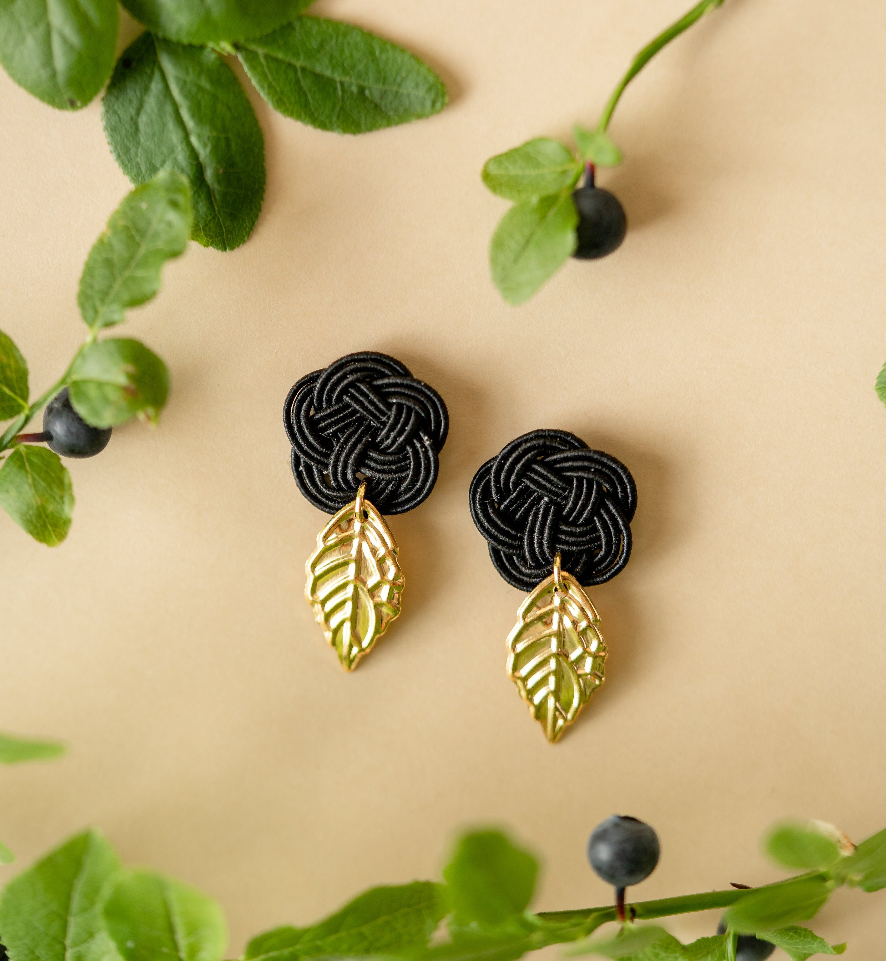 Close-up of earrings with a black plum  knot and gold leaves, handmade by Itookasi.