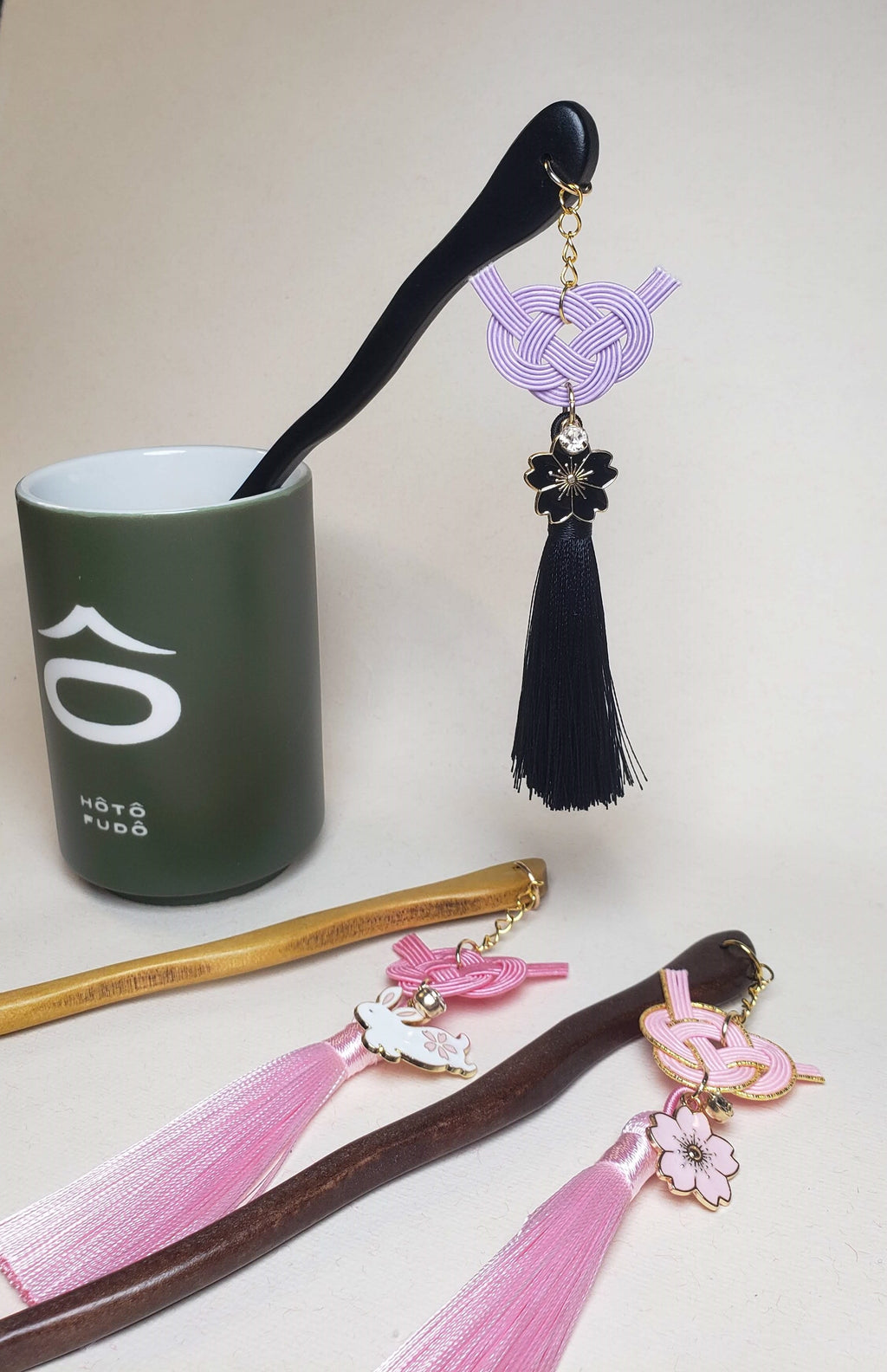 Close-up of pink and purple Japanese Kanzashi hair ornament featuring red Mizuhiki Awaji knots with a tassel and Sakura charm. Handmade by Itookasi.