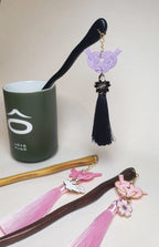 Close-up of pink and purple Japanese Kanzashi hair ornament featuring red Mizuhiki Awaji knots with a tassel and Sakura charm. Handmade by Itookasi.