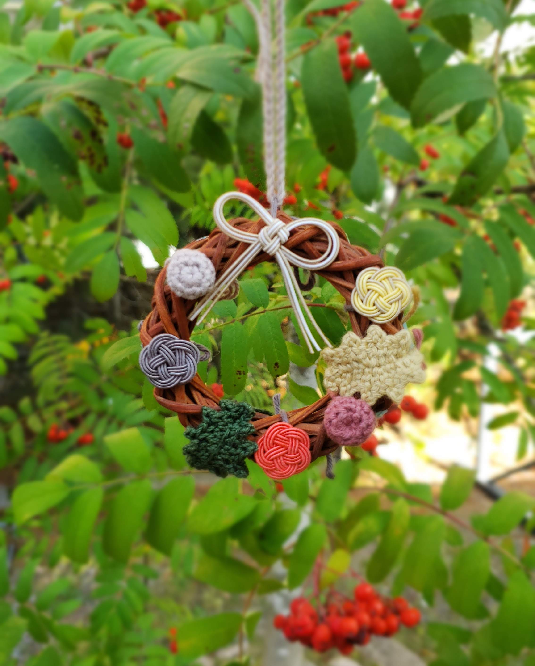 Close-up of a Christmas wreath adorned with a plum knot made of mizuhiki against a backdrop of trees, handmade by Itookasi.