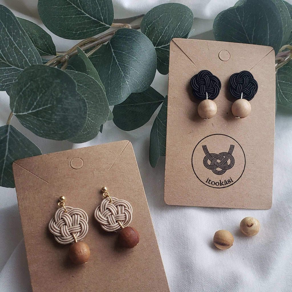 Close-up of black and beige Mizuhiki Ume (Plum Blossom) knot earrings with Finnish wood beads, handmade by Itookasi. A blend of Japanese craft and Finnish nature symbolizing strong bonds.