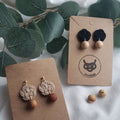Close-up of black and beige Mizuhiki Ume (Plum Blossom) knot earrings with Finnish wood beads, handmade by Itookasi. A blend of Japanese craft and Finnish nature symbolizing strong bonds.