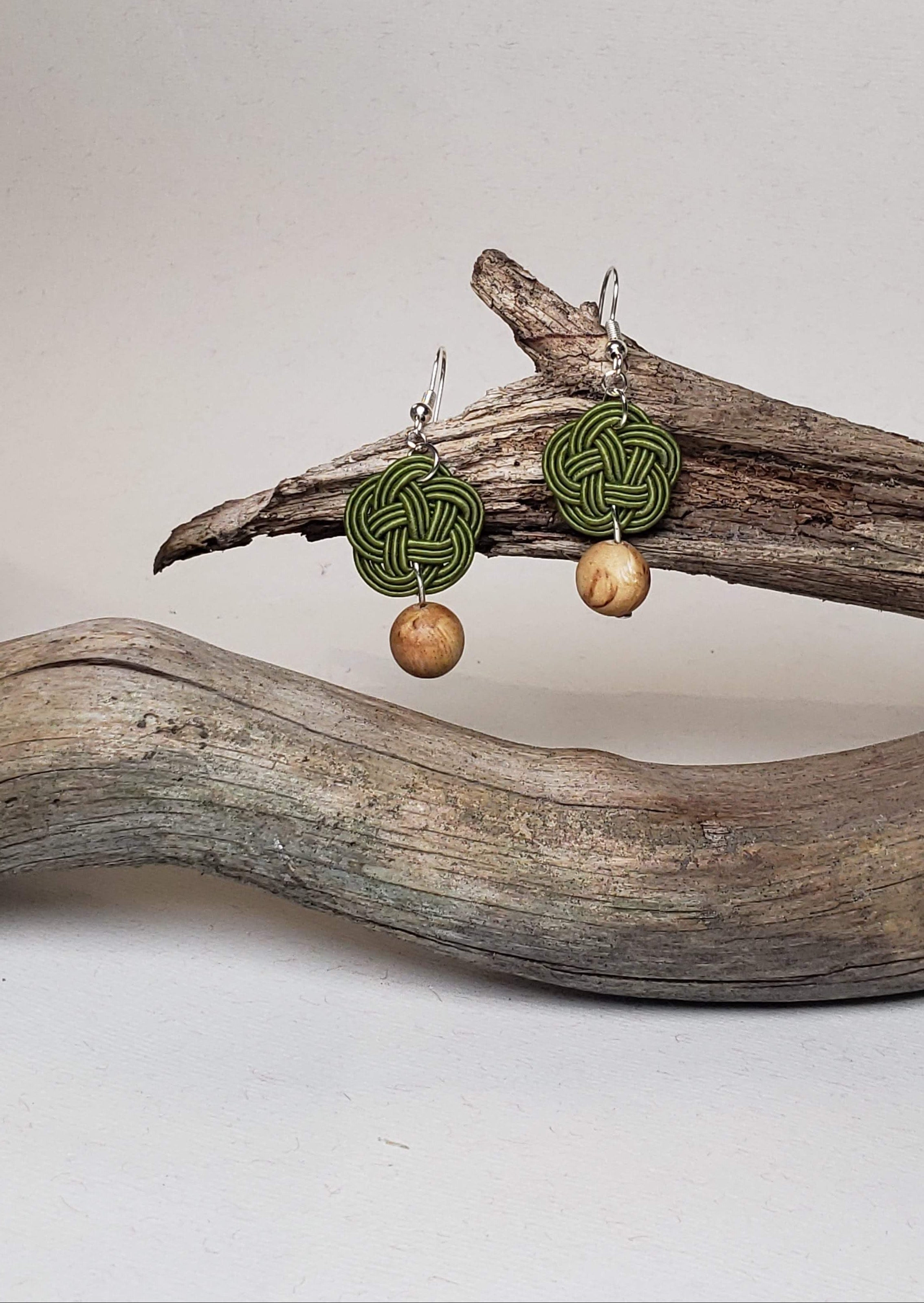 Close-up of olive green Mizuhiki plum knot earrings with Finnish wood beads, handmade by Itookasi. A blend of Japanese craft and Finnish nature symbolizing strong bonds.