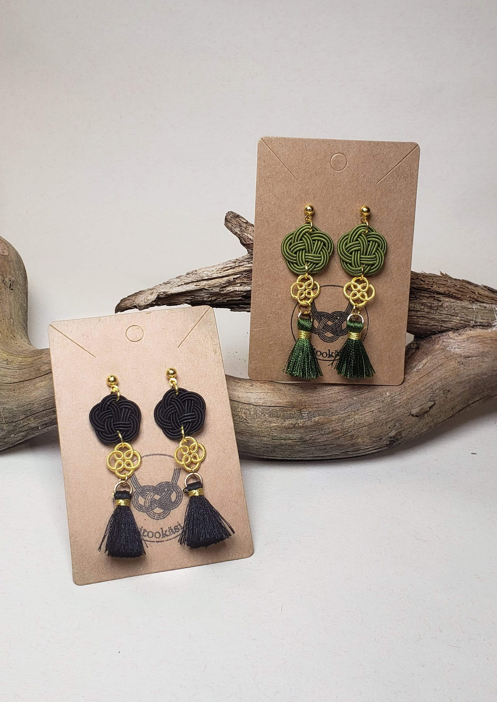 Close-up of black and green Mizuhiki plum knot earrings with matal flower charm and small tassel, handmade by Itookasi. A blend of Japanese craft and Finnish nature symbolizing strong bonds.