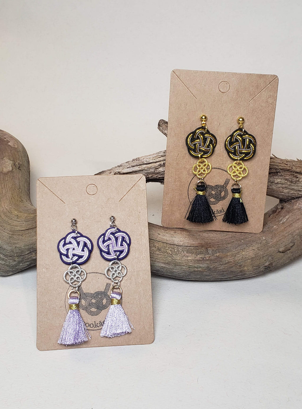 Close-up of black and gold black Mizuhiki plum knot earrings with matal flower charm and small tassel, handmade by Itookasi. A blend of Japanese craft and Finnish nature symbolizing strong bonds.