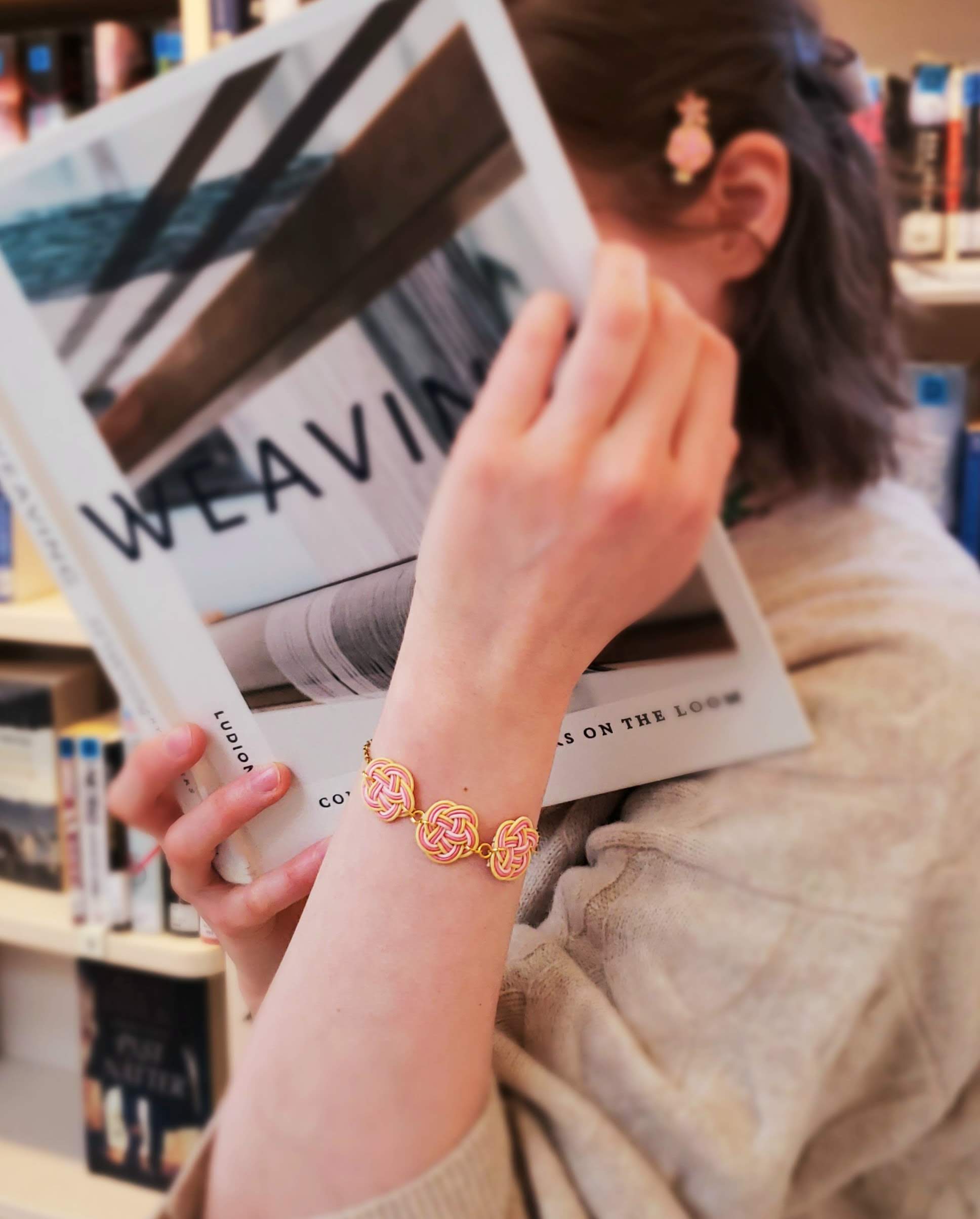 Close-up of a woman reading a book, wearing a yellow and pink mizuhiki plum knot bracelet and a small hair clip, handmade by itookasi.